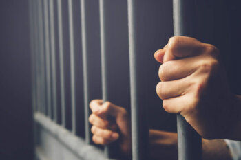 Man in prison hands of behind hold Steel cage jail bars. offende