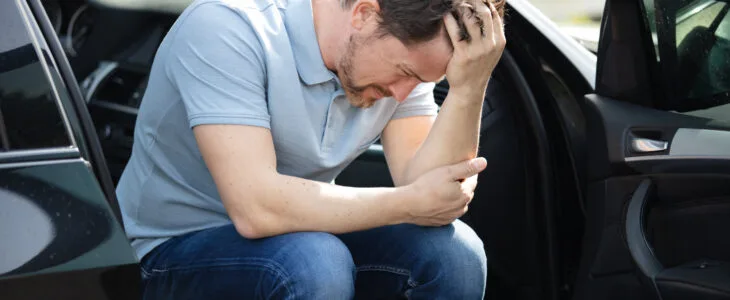 A man hunched over in his car after a crash, showing the pain and warning signs of delayed symptoms after a car accident.