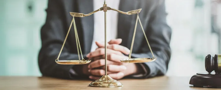 A lawyer sits at a desk beside the scales of justice, representing the question many people ask about what is a tort attorney and their role in personal injury cases.