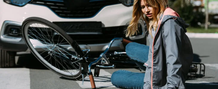 A woman lies on the street beside her bicycle after being struck by a car at a crosswalk, showing the aftermath of a bicycle car accident insurance claim situation.