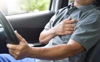 A man sits in the driver’s seat holding his chest in pain, representing the warning signs of chest pain after car accident injuries.