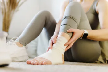A woman holds her bandaged ankle in pain, representing the factors that can raise soft tissue injury claim value.