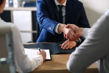 A lawyer shakes hands with a client at a desk, representing discussions about what percentage do lawyers take for personal injury cases.